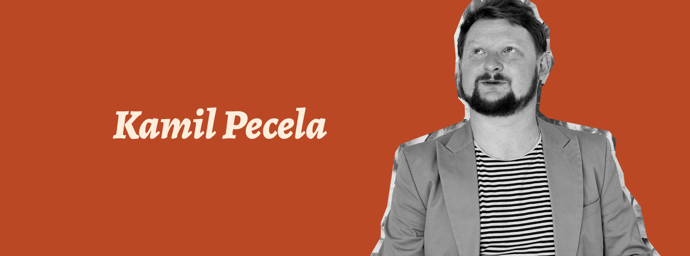 Kami Pecela czarno-biały stylizowany portret tłumacza Kamila Peceli. to młody mężczyzna z krótkimi, gęstymi rudymi włosami, wąsami i brodą. Zdjęcie przedstawia jego sylwetkę do pasa. Patrzy do góry, lekko w lewo, poza kadr. ubrany jest w szara marynarkę i bluzę w paski z okrągłym dekoltem