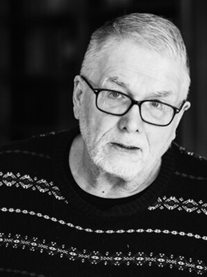 Berzins_Uldis czarno-biały stylizowany portret łotewskiego pisarza Uldis Berznis. To starszy mężczyzna, z krótkimi, siwymi włosami, brodą i okularami. Ma na sobie bluzę rozpinana ze stójką.