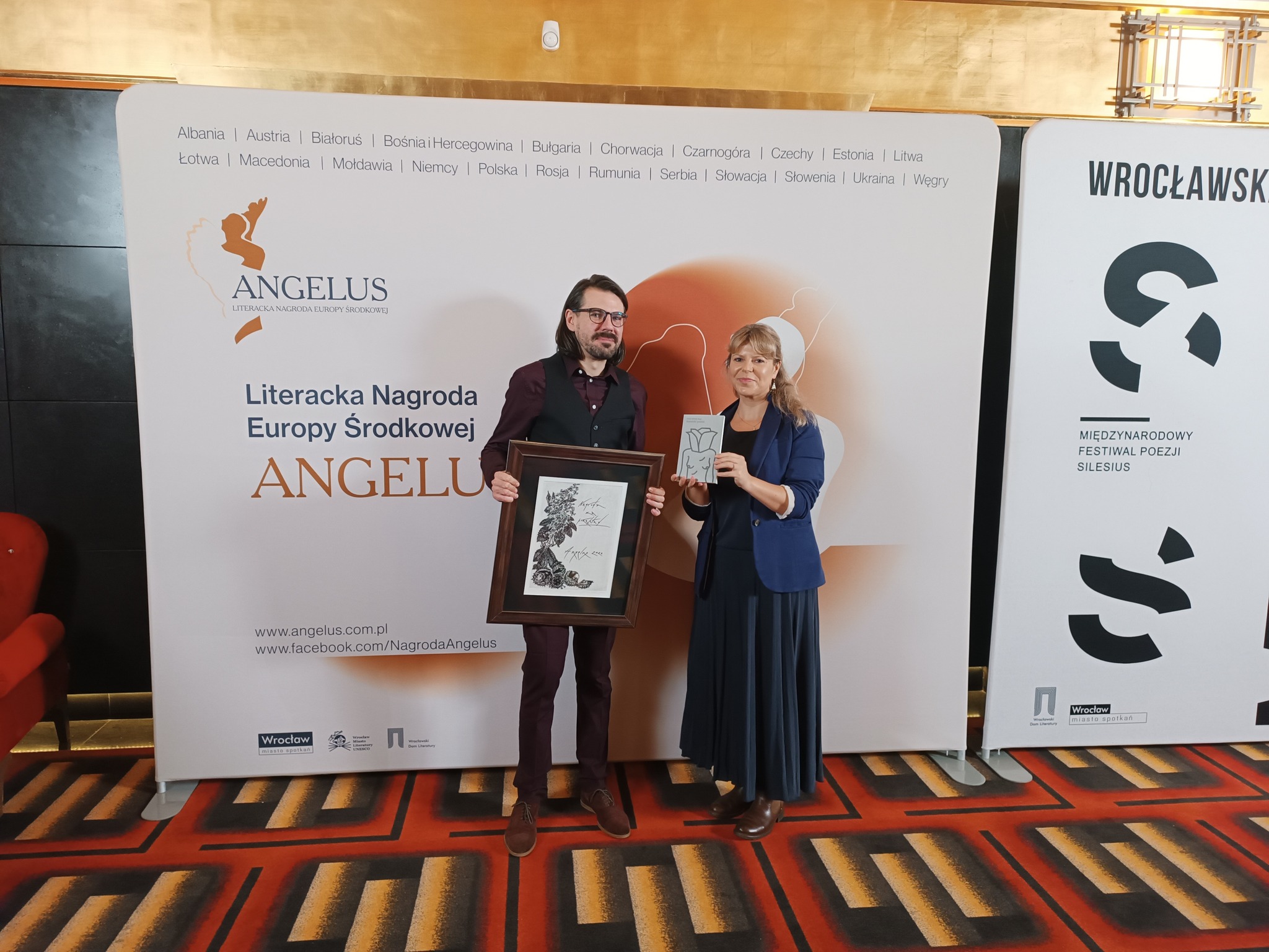 Dwie osoby na ściance ANGELUS. Daniel warmuz z nagrodą Angelusa za tłumaczenie ksiazki "Szatański pomiot"